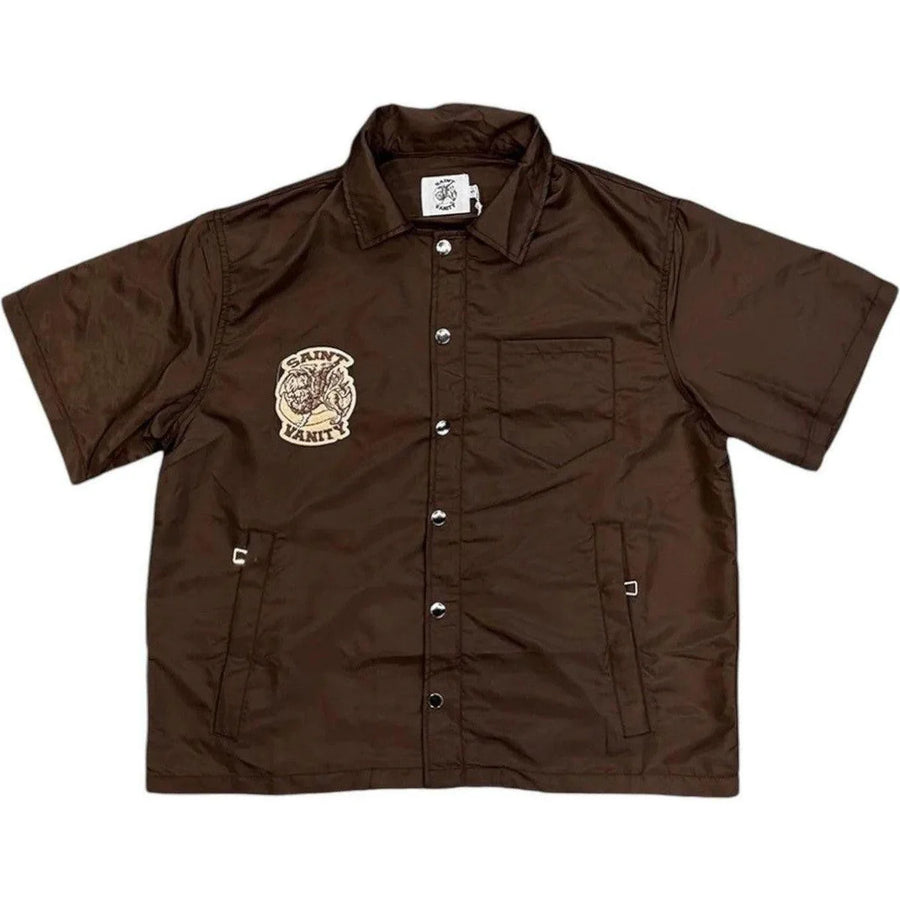 Brown nylon short-sleeve collared shirt with Saint Vanity logo patch, silver snap buttons, chest pocket, and two zippered pockets.