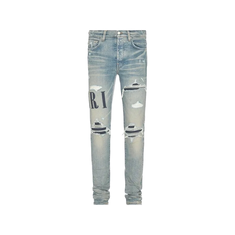 AMIRI Clay Indigo distressed jeans. Faded light blue with large 'AMIRI' appliqué logo & ripped knees revealing striped fabric.