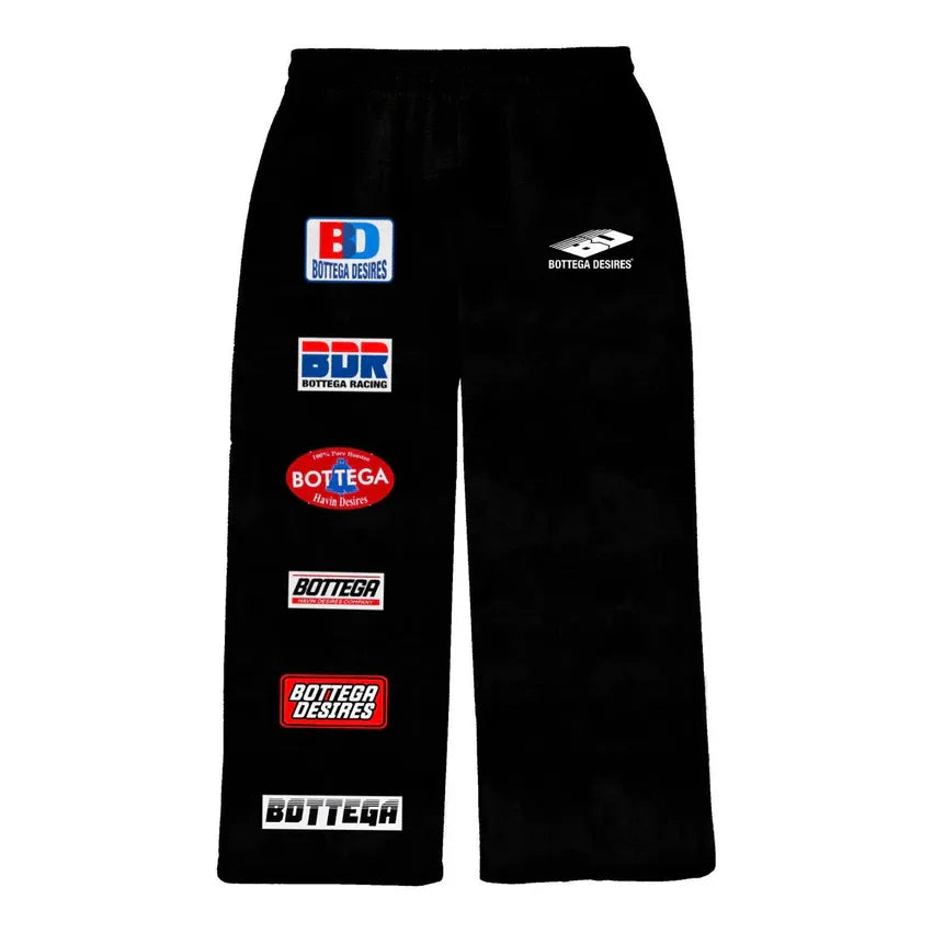 Black Bottega Desires sweatpants with multiple colorful brand logo patches on the left leg and one small white logo on the right.