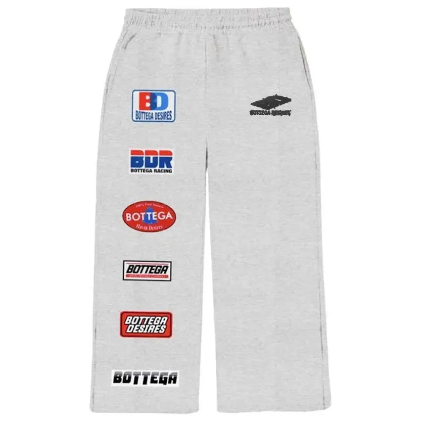 Grey Bottega Desires sweatpants, featuring multiple colorful racing-style brand logo patches down the left leg.