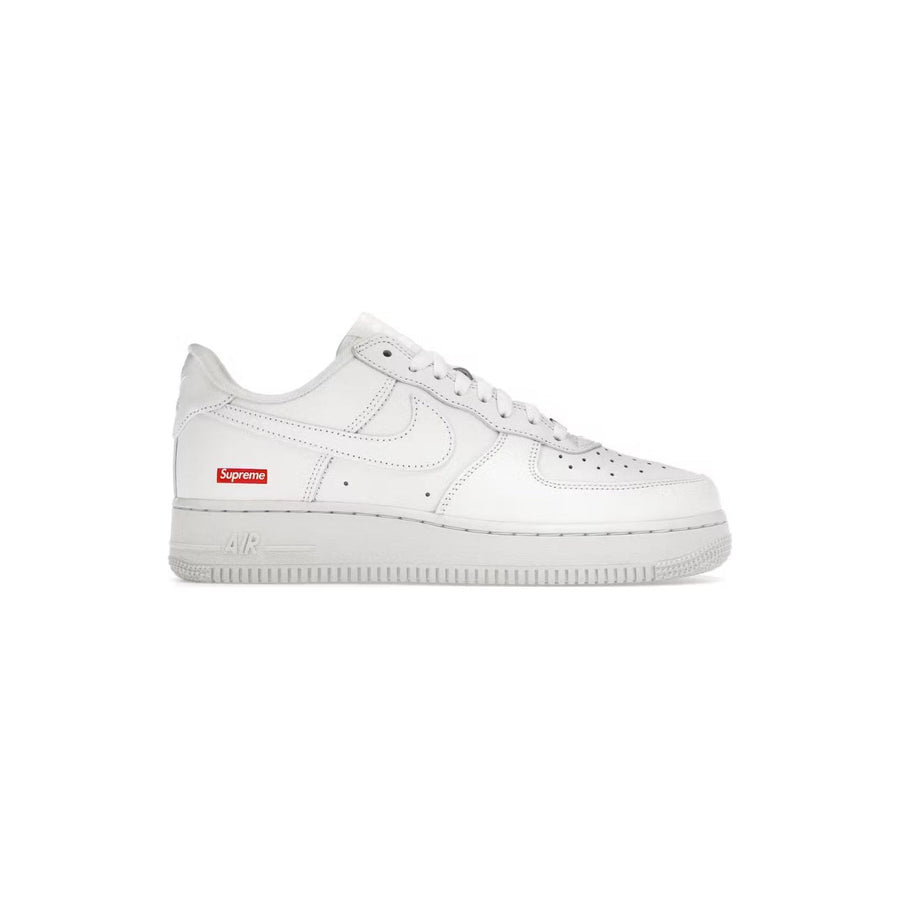 White Nike Air Force 1 Low x Supreme sneaker. White leather, white Swoosh, red Supreme box logo on heel, 'AIR' text on midsole.