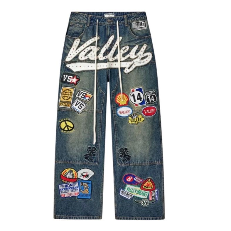Vale Forever 1980 distressed blue painter jeans with large studded "Valley" text and many colorful brand patches.