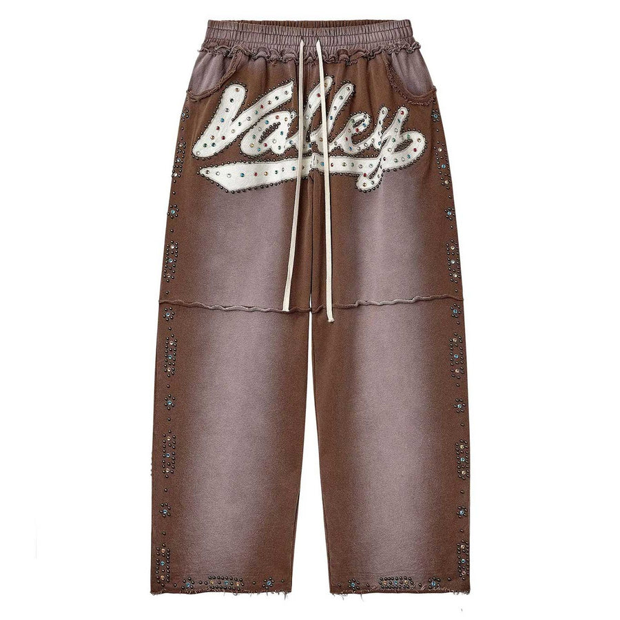 Brown sweatpants with "Valley" in white, colorful Skittles studs, elastic waist, drawstring, and raw hem.