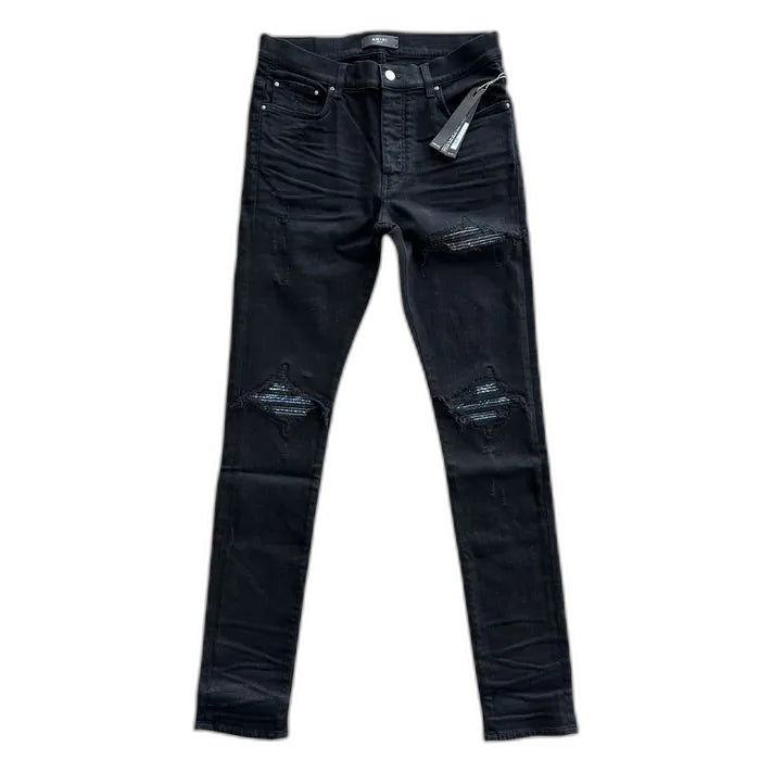 AMIRI MX1 black skinny jeans featuring ripped knees with multicolored paisley exclusive patches underneath.
